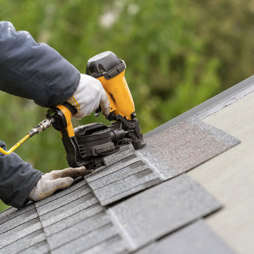 Workman Using Pneumatic Nail Gun Install Tile On Roof Of New House Under Construction